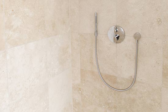 Dusche in hellem Naturstein. Auf dem Boden der niveaugleichen Dusche wurden die Platten in ein kleineres Format geschnitten um durch den erhöhten Fugenanteil eine größere Rutschsicherheit zu erhalten. Der Ablauf ist durch eine Rinne ausgebildet und fügt sich harmonisch ein.